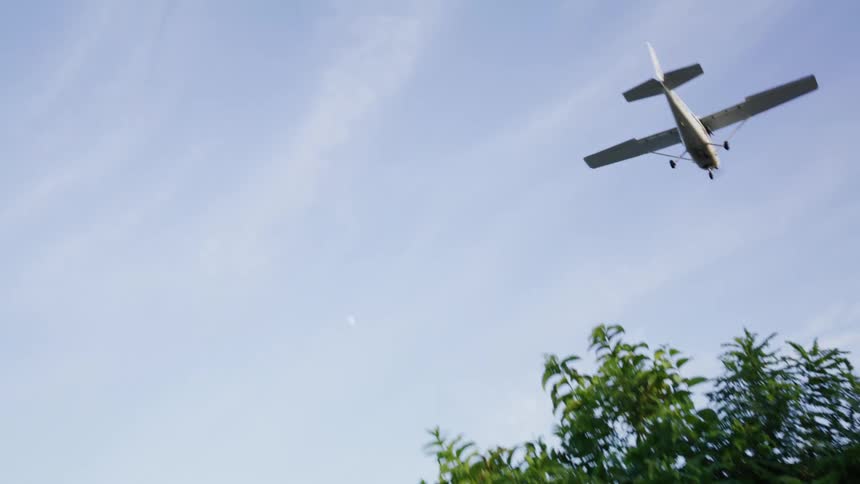 Airplane flies over field through cloudy sky