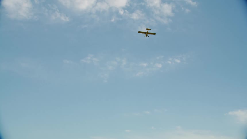 A small airplane flies overhead under a blue sky with scattered clouds in it