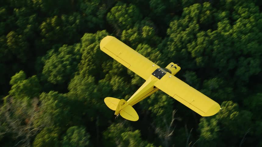 Bright yellow colored airplane flies over woods and winding roads
