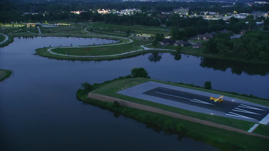 Yellow singleengine plane landing on a lakeside runway at dusk