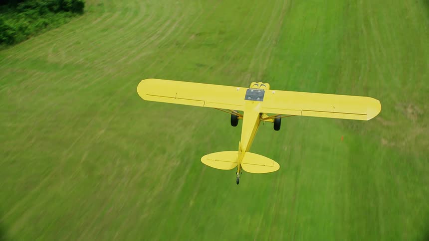 Yellow airplane flies over field with hay bales in rural countryside