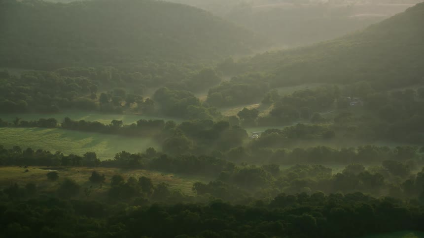 Fog covers rural countryside between forested mountains