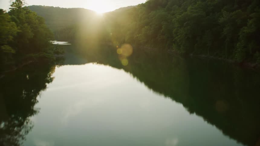 Landscape of a river surrounded by forests and the suns reflection on the horizon