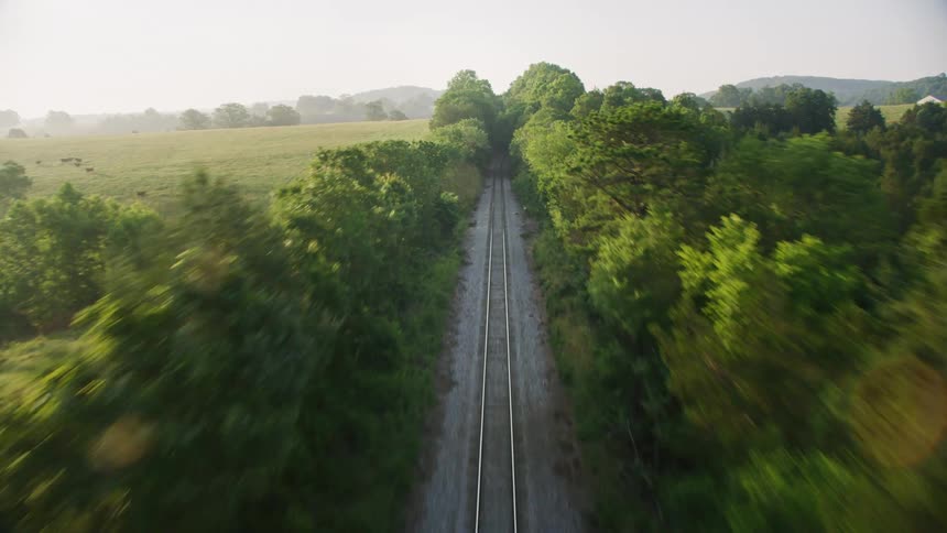 Aerial of hidden railroad tracks going through trees in the countryside