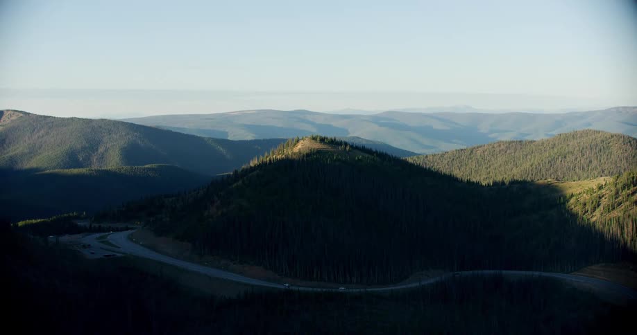 Vehicles drive on highway passing through shadow covering forested mountain in mountain range on a foggy day