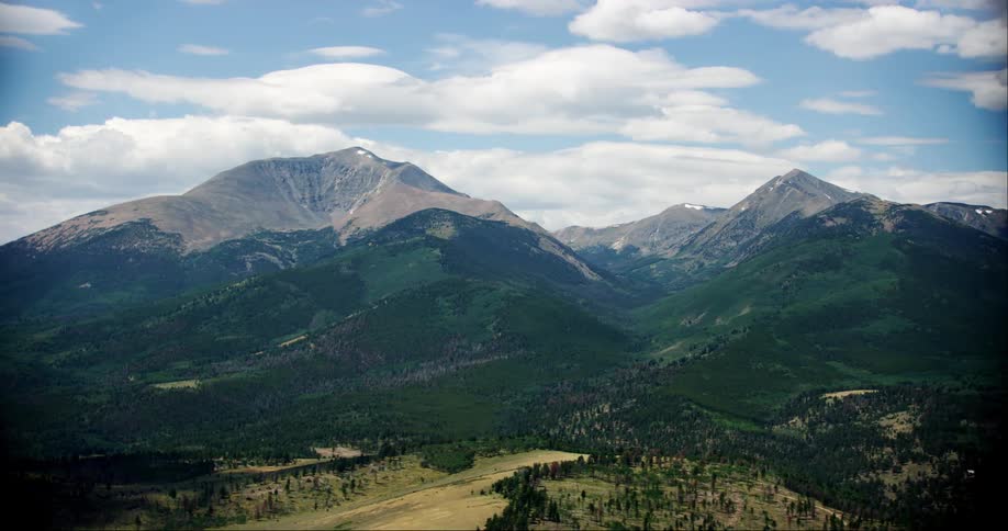 A mountain range towers over a valley filled with forests and small plains