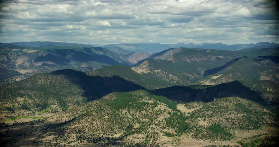 An aerial view of a mountainous region with some hills with undergrowth and white clouds in the sky