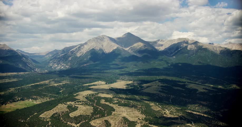 Aerial landscape of hills and mountain ranges with cliffs and greenish forest in a blue sky with clouds
