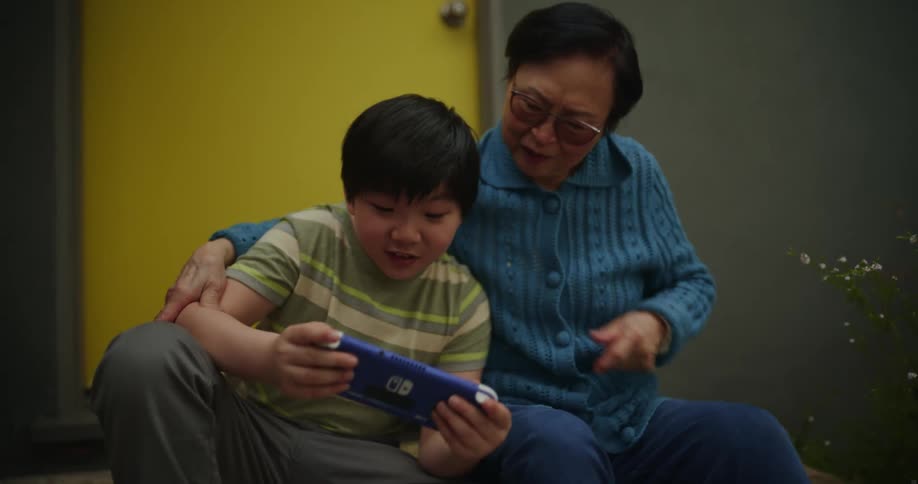 Grandmother hugging her grandson while playing on a portable game and both talking smiling