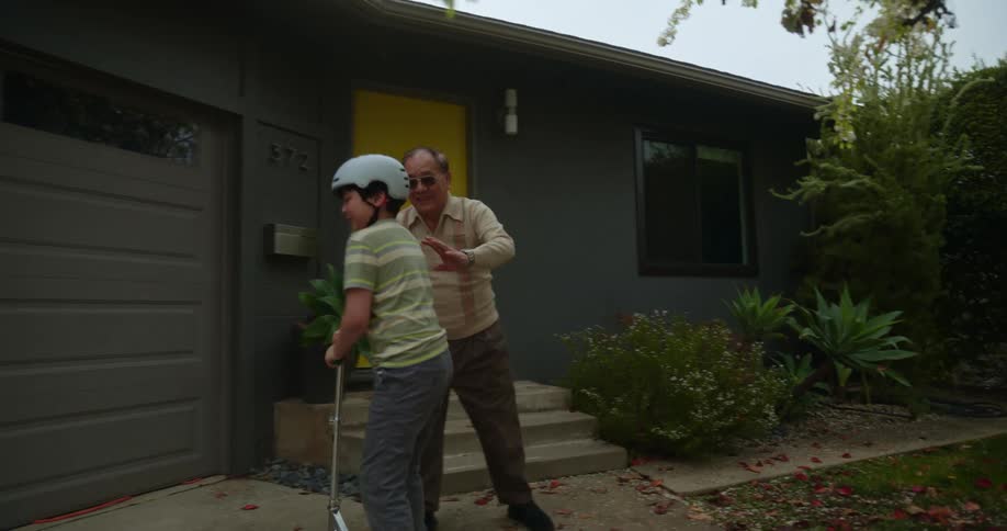 Young asian boy riding a scooter while grandfather gently pushes him