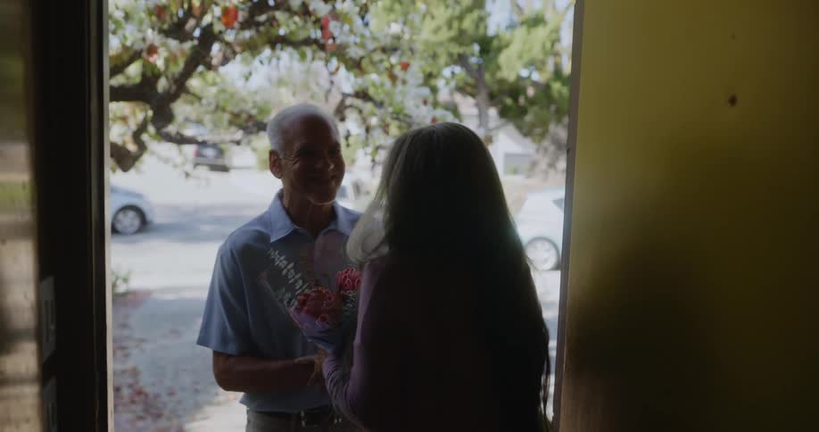 A woman opens a door and accepts flowers from a man