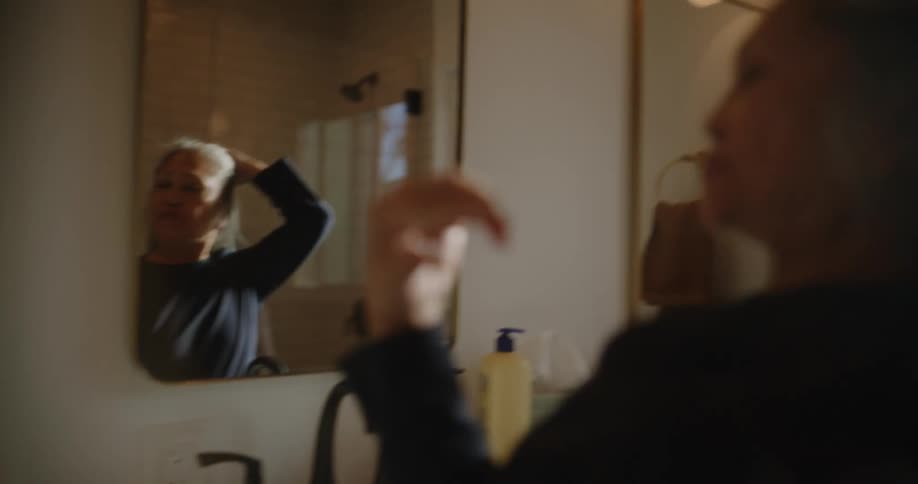 Woman moving her hair and looking at herself in the mirror with a happy expression