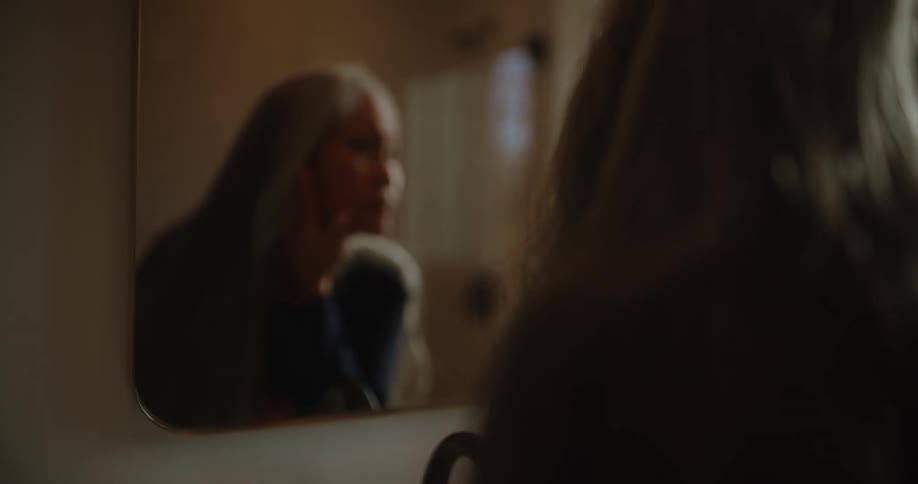 Elderly woman examines her face while looking in the bathroom mirror