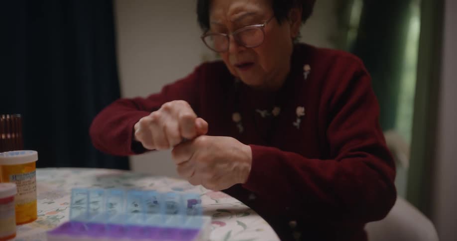 Elderly woman sitting at a table struggling to open a medicine