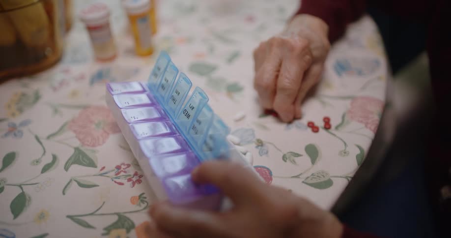 Hands of an elderly woman placing medicine capsules in a jar with dividers