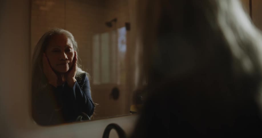 A woman is rubbing her face in the mirror