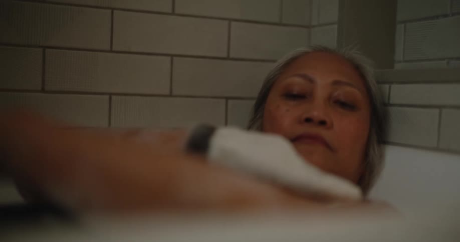 Asian woman washes herself in the bathtub with bubbles and a loofah glove