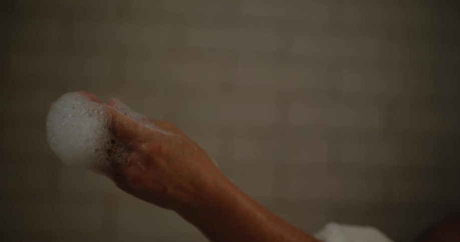 Woman lying in the bathtub washing her arm with a hand sponge