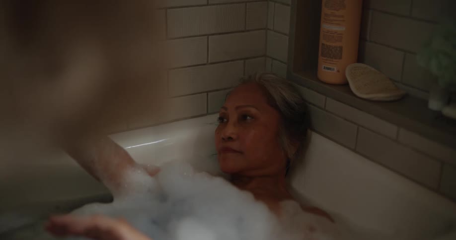Elderly woman lying in a bathtub relaxing while running her hands over her face