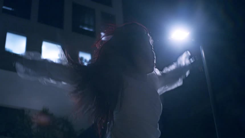 A young woman performs a dance outside a building at night