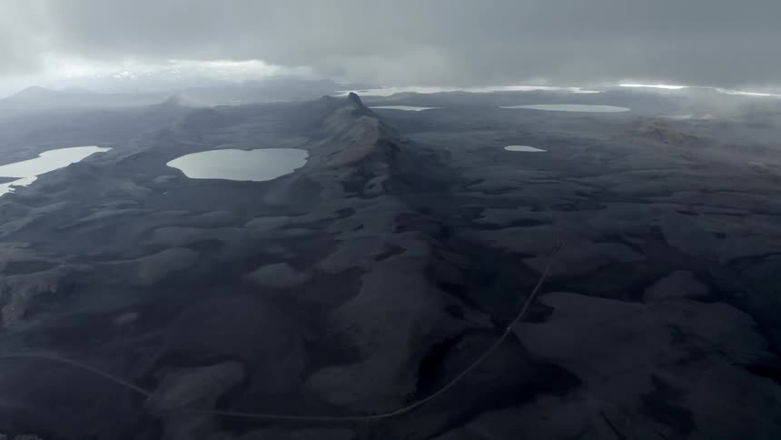 Small lakes in black rocky craters on a cloudy day