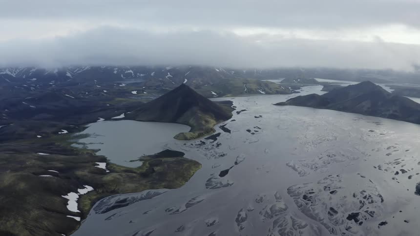 An aerial view of a lake surrounded by mountains with peaks under the clouds