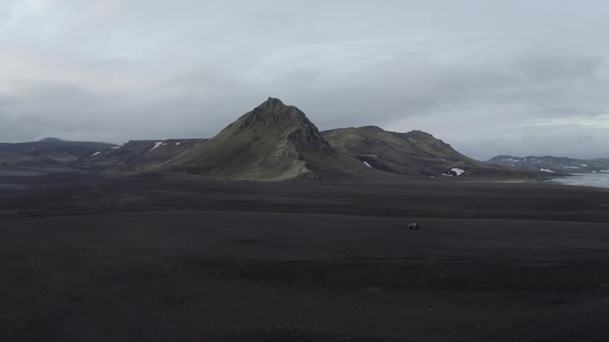A vehicle drives across flat terrain near mountains