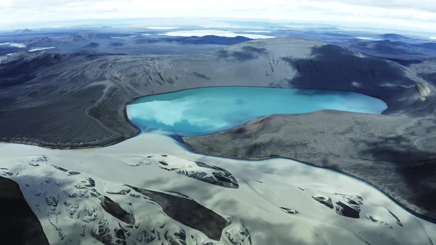 Aerial landscape of a blue lake in a crater on a mountain and with flakes of snow around