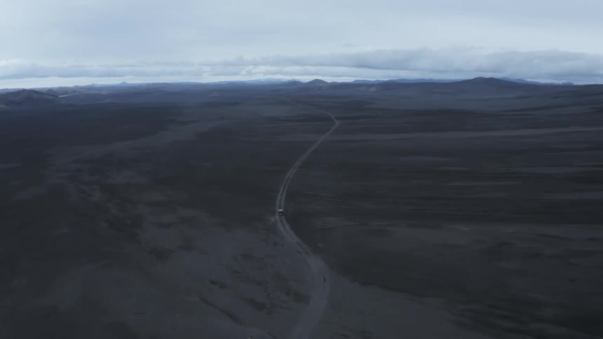 A vehicle drives down a long road on a plain
