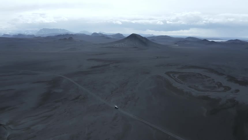 Aerial panorama of a vehicle traveling along a dirt road and a desert terrain with hills and mountains on the horizon