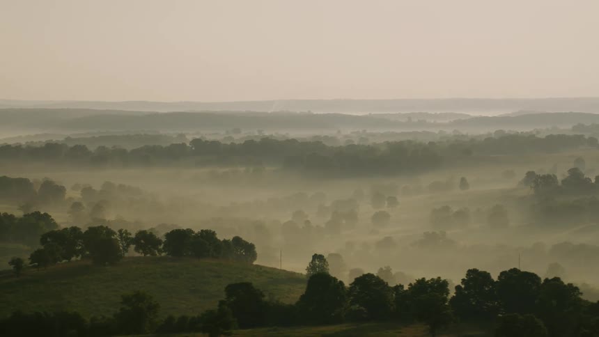 Line of utility poles stand in fog covered hilly terrain under a red tinted sky