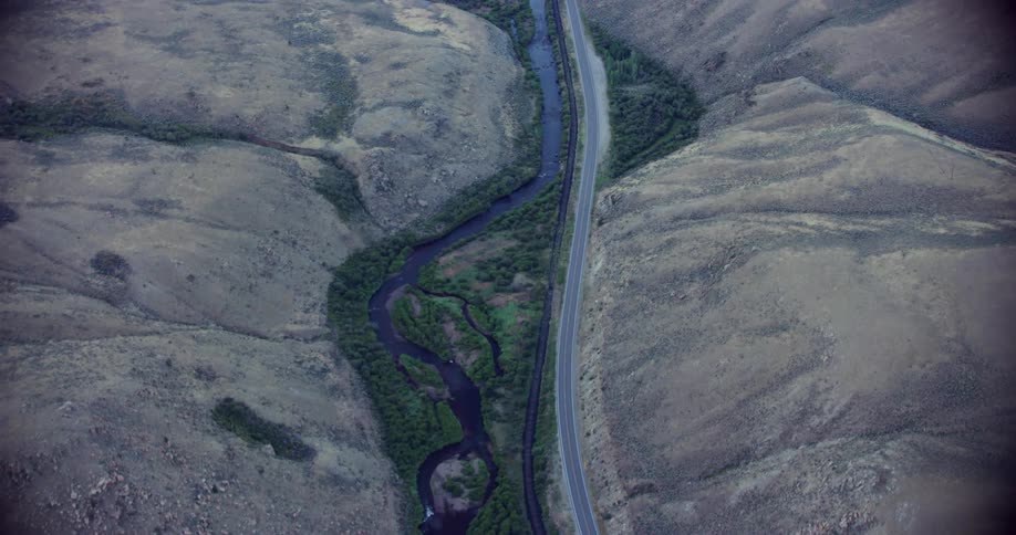 Aerial panorama of a highway in the middle of hills and mountains on the edge of a river canal
