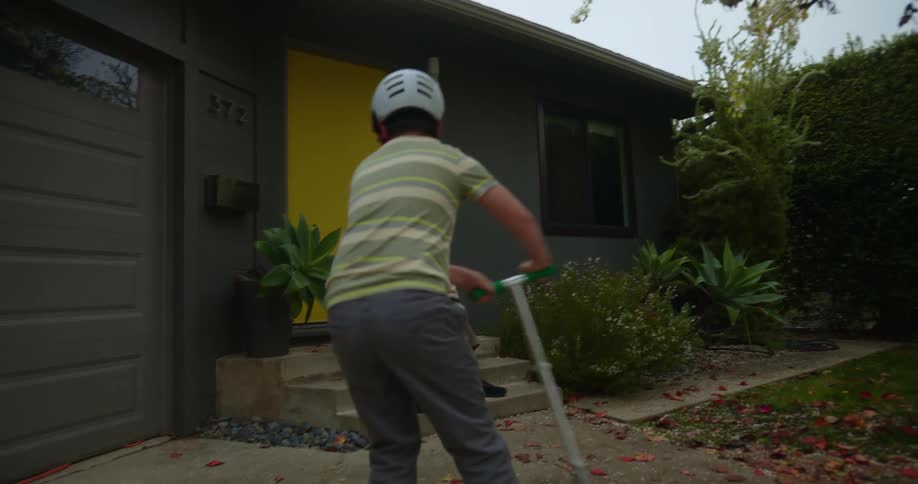 Grandfather watches grandson play with scooter then sits with him on house stoop