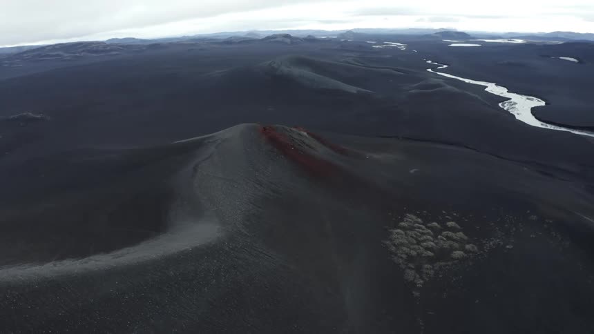 Red stains gray tinted mountain slope near river winding through hilly terrain