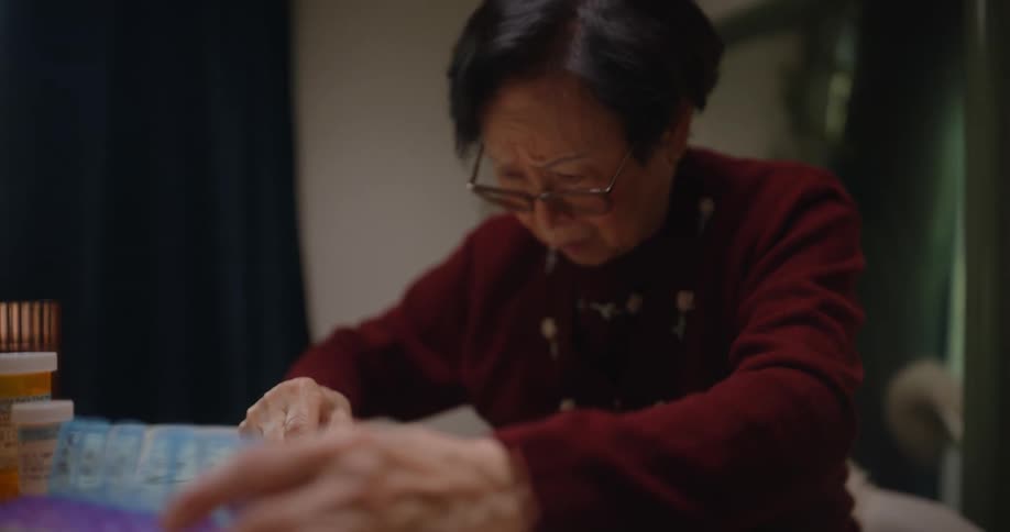 Elderly lady sitting at table organizing medicine capsules