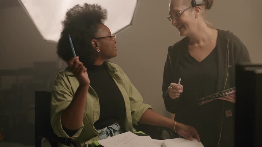 Two women with one of them sitting and talking inside a studio