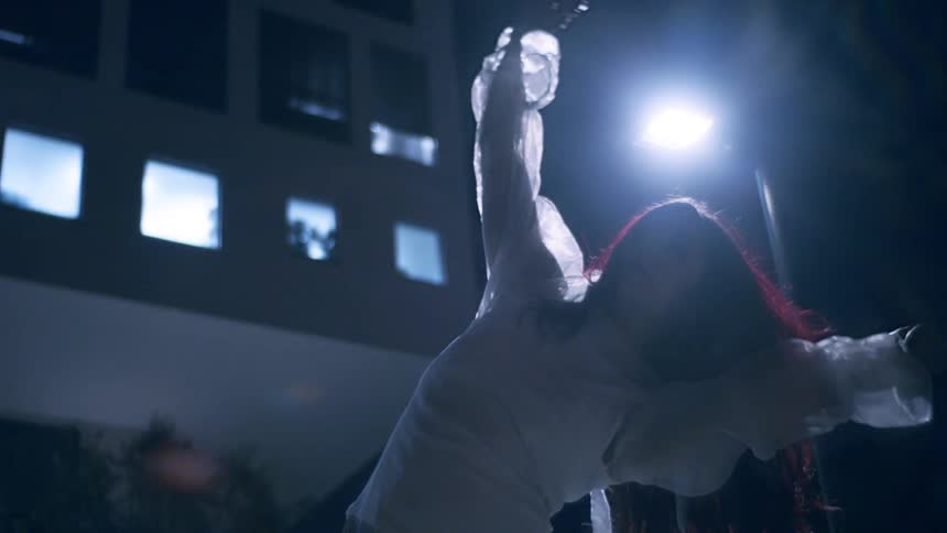 A woman wearing a white translucent shirt dances in the night
