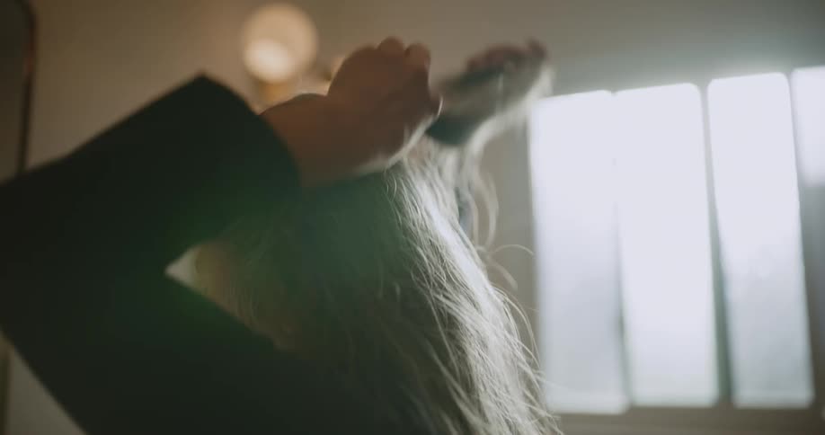 An asian woman fixes her hair with a hair clip while looking in a bathroom mirror
