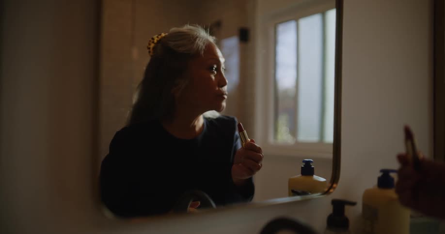Elderly woman applies lipstick in front of a mirror at morning