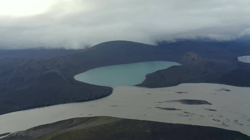 Aerial landscape of a bluish lake in a crater amid snowy mountains on a cloudy day
