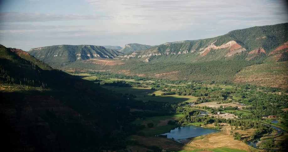 Rural farmland valley surrounded by green mountain hillsides half bright and sunny and half dark and shadowed