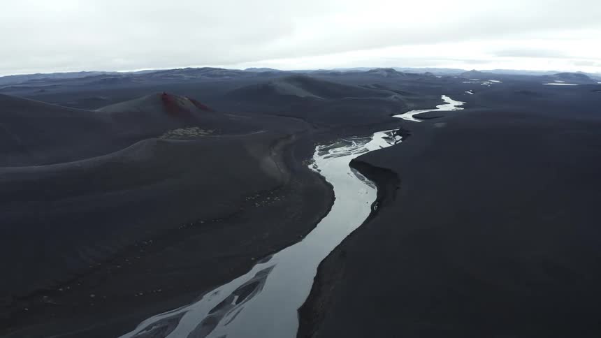 Aerial panorama of a river and a half of black desert soil on a cloudy day