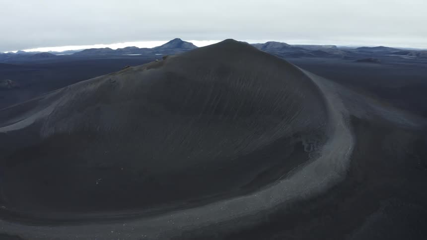 Aerial landscape of a mountain on a black desert floor with slopes and cliffs on a cloudy morning