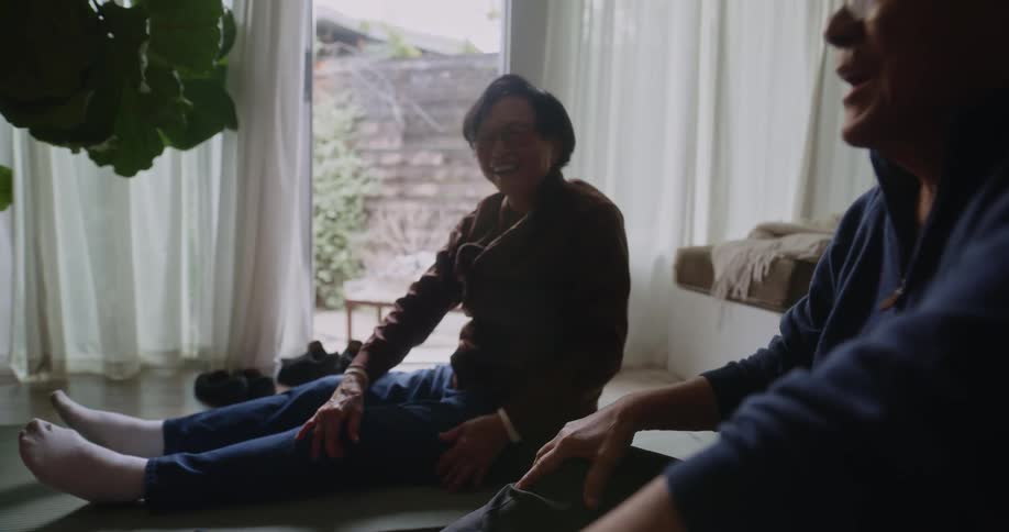 Elderly couple smiles while they move through yoga stretch at home