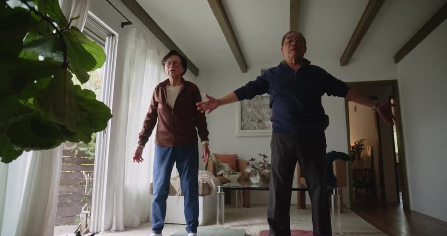 Elderly man and woman standing in room stretching their arms and color