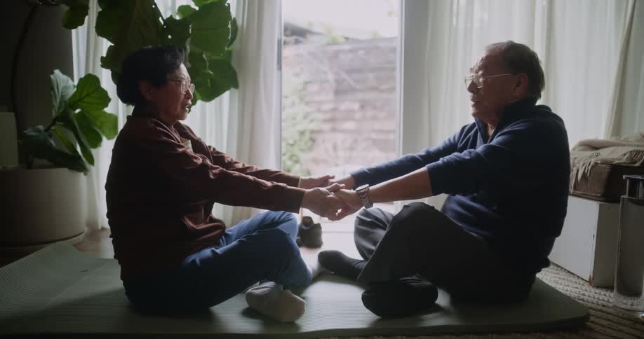 Elderly couple sitting on a rug holding hands stretching each others bodies
