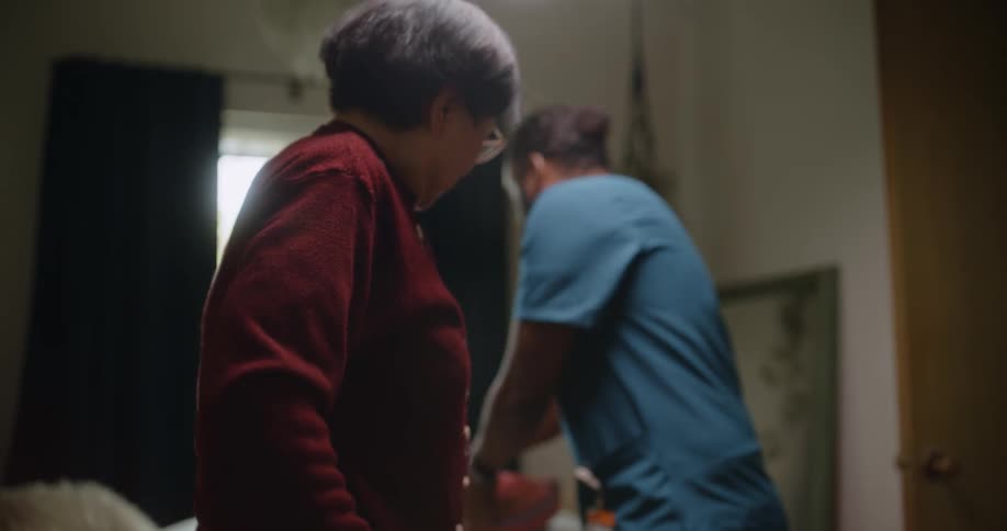 Professional caregiver hands elderly asian woman her purse and assists her from the room