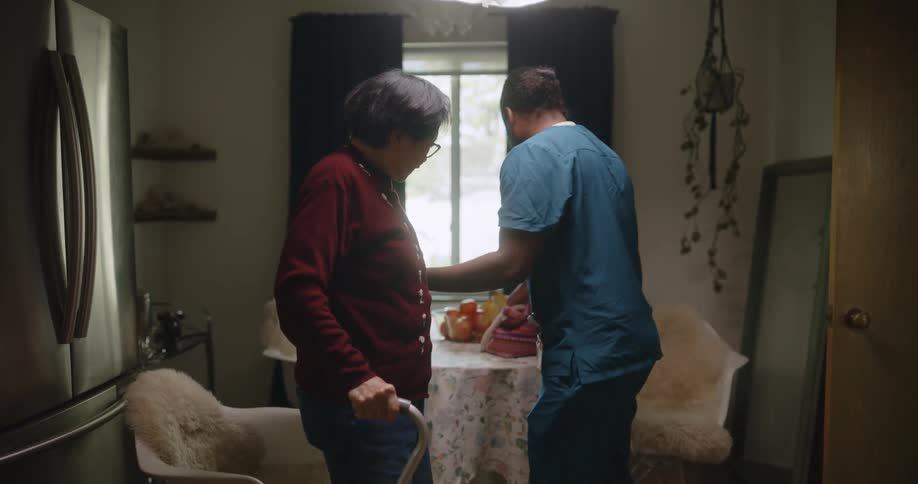 A healthcare worker helps a patient walk out of the room