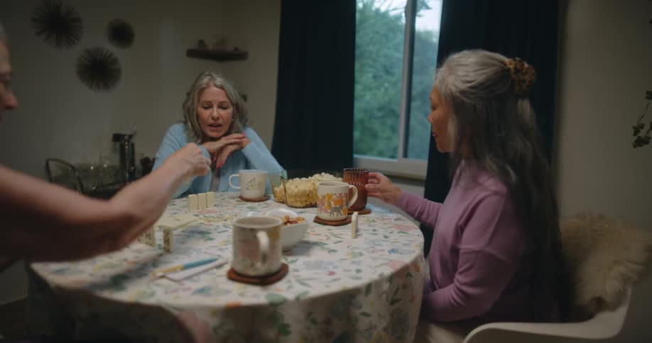 Friends sitting at a table eating and drinking from a cup while playing dominoes
