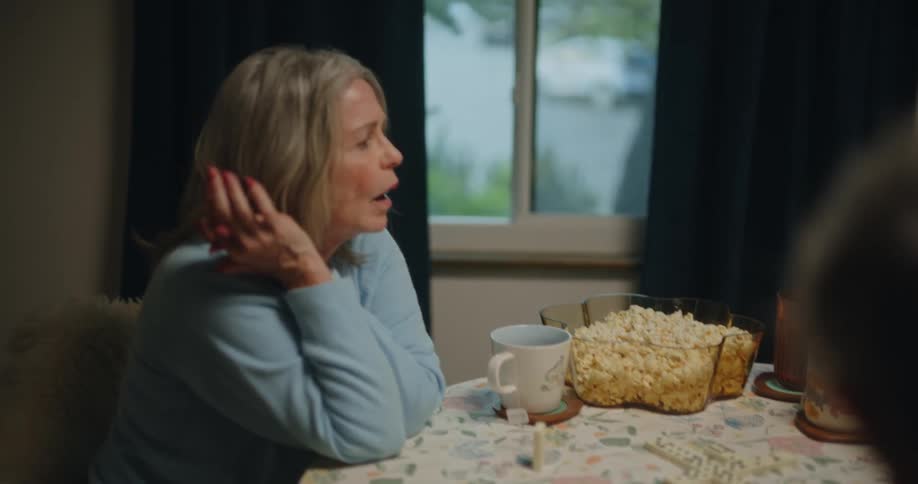 Female friends play dominoes at a table with multiple snacks